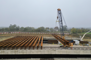 The beams, each weighing up to 105 tonnes, are being lifted into place in pairs. These beams will form the foundation for a concrete deck constructed with pre-cast slabs. Once completed, the deck will support 2,700 cubic metres of earth, forming the final landscaped structure.