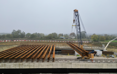 The beams, each weighing up to 105 tonnes, are being lifted into place in pairs. These beams will form the foundation for a concrete deck constructed with pre-cast slabs. Once completed, the deck will support 2,700 cubic metres of earth, forming the final landscaped structure.